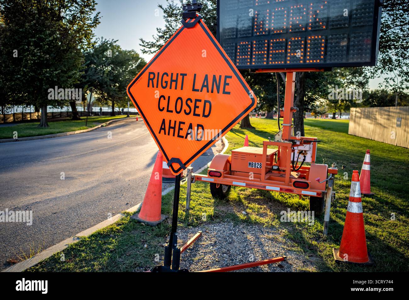 Tidal Basin Construction Site Road cartelli per Washington DC // WASHINGTON DC — Un cartello stradale "RIGHT LANE CLOSED AHEAD" e una bacheca elettronica sono esposti in un cantiere di Tidal Basin. Questi cartelli e attrezzature temporanei indicano lavori stradali in corso e chiusure di corsie per progetti di riabilitazione. Il bacino delle maree, un'insenatura artificiale di Washington DC, sta subendo significativi miglioramenti infrastrutturali. Questi progetti mirano a risolvere problemi come l'innalzamento del livello del mare, il fallimento dei banchi marittimi e migliorare l'accesso dei visitatori. L'area è un punto di riferimento importante, circondato da ciliegi e monumenti nazionali. Foto Stock