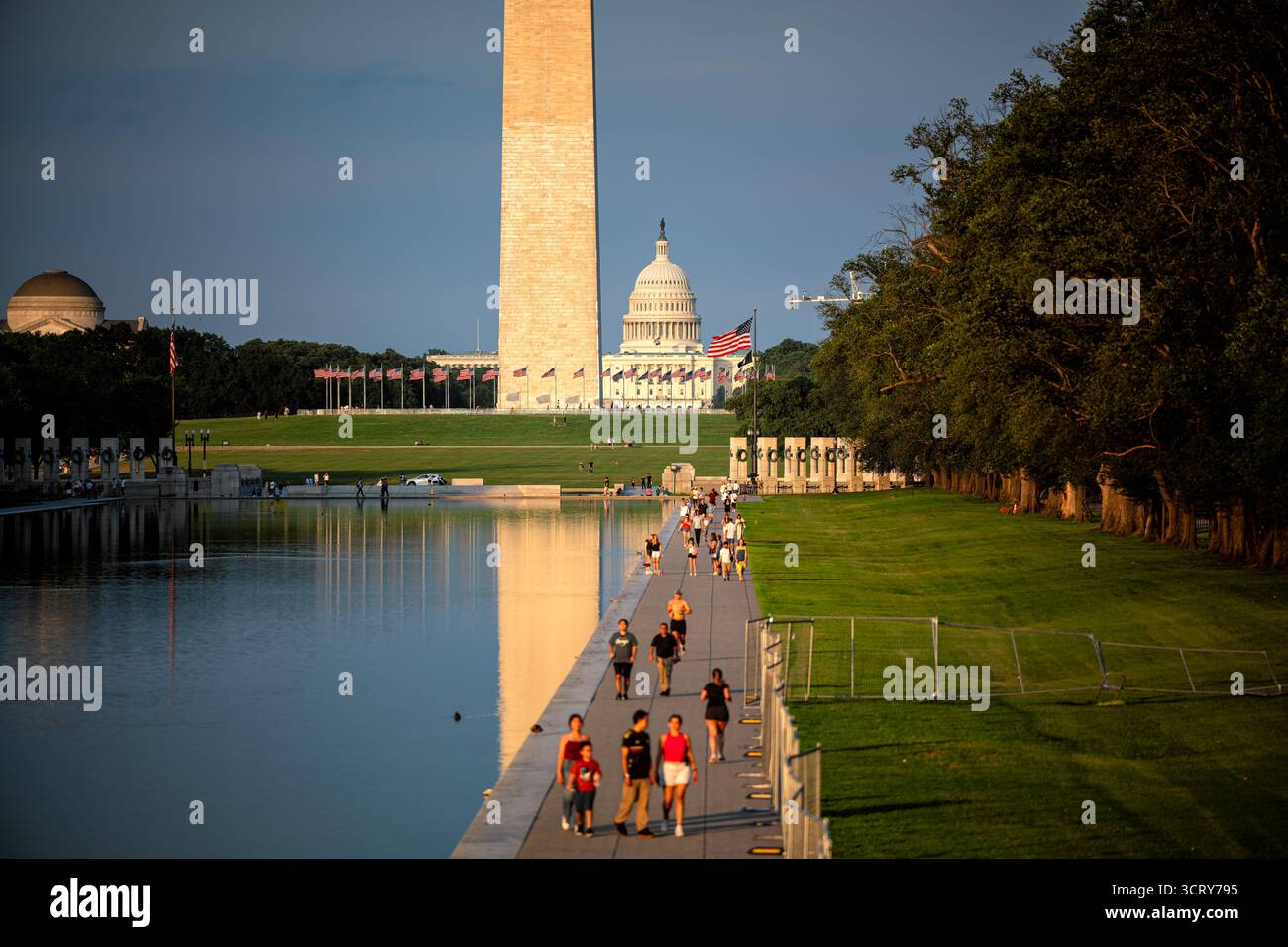 Monumento a Washington e Capitol Building National Mall Washington DC // WASHINGTON DC - il monumento a Washington e il Campidoglio degli Stati Uniti sono ben visibili attraverso la piscina riflettente del National Mall. I pedoni passeggiano lungo il bordo della piscina, con il World War II Memorial e numerose bandiere americane visibili. I luoghi di interesse più rappresentativi sono immersi nella luce dorata di una sera estiva limpida, appena prima del tramonto. Il National Mall è un importante parco nazionale e spazio civico nel centro di Washington DC. Foto Stock