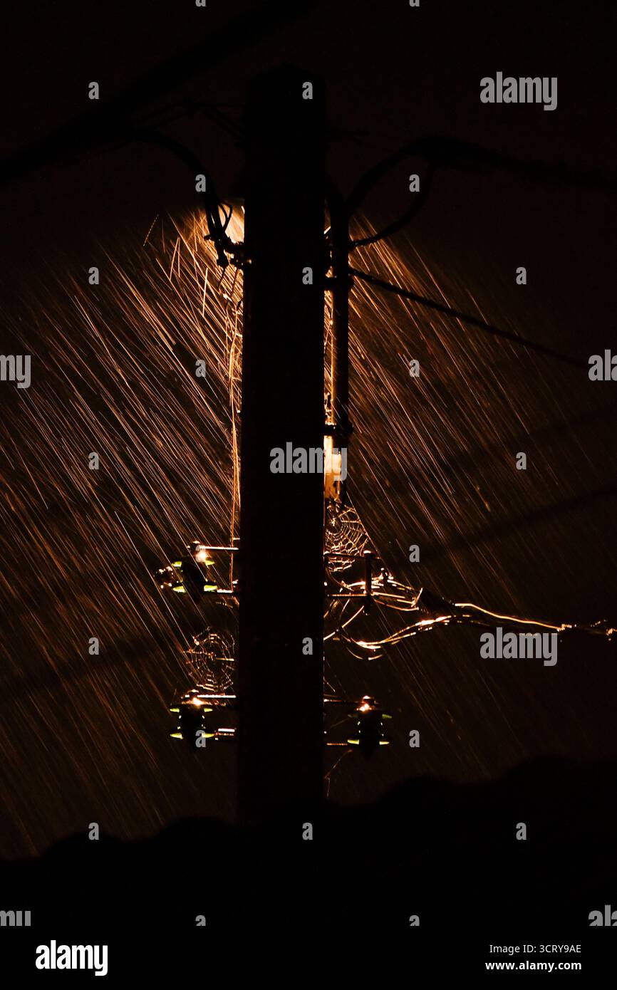 Pioggia intensa che cade nell'illuminazione atmosferica contro un lampione del telegrafo. Foto Stock