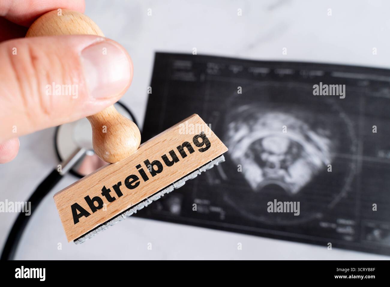 Bavaria, Germania - 3 ottobre 2025: FOTOMONTAGGIO, foto simbolica sull'aborto: Un timbro di legno con l'iscrizione davanti ad un'immagine a ultrasuoni, raffigurata come riferimento alla tensione medica e legale che circonda l'aborto *** FOTOMONTAGE, Symbolfoto zur Abtreibung: Ein Holzstempel mit der Aufschrift vor einem Ultraschallbild, dargestellt als Hinweis auf und Schfschaftschandschandschandsund Spungtschandschandschandsdav v Foto Stock
