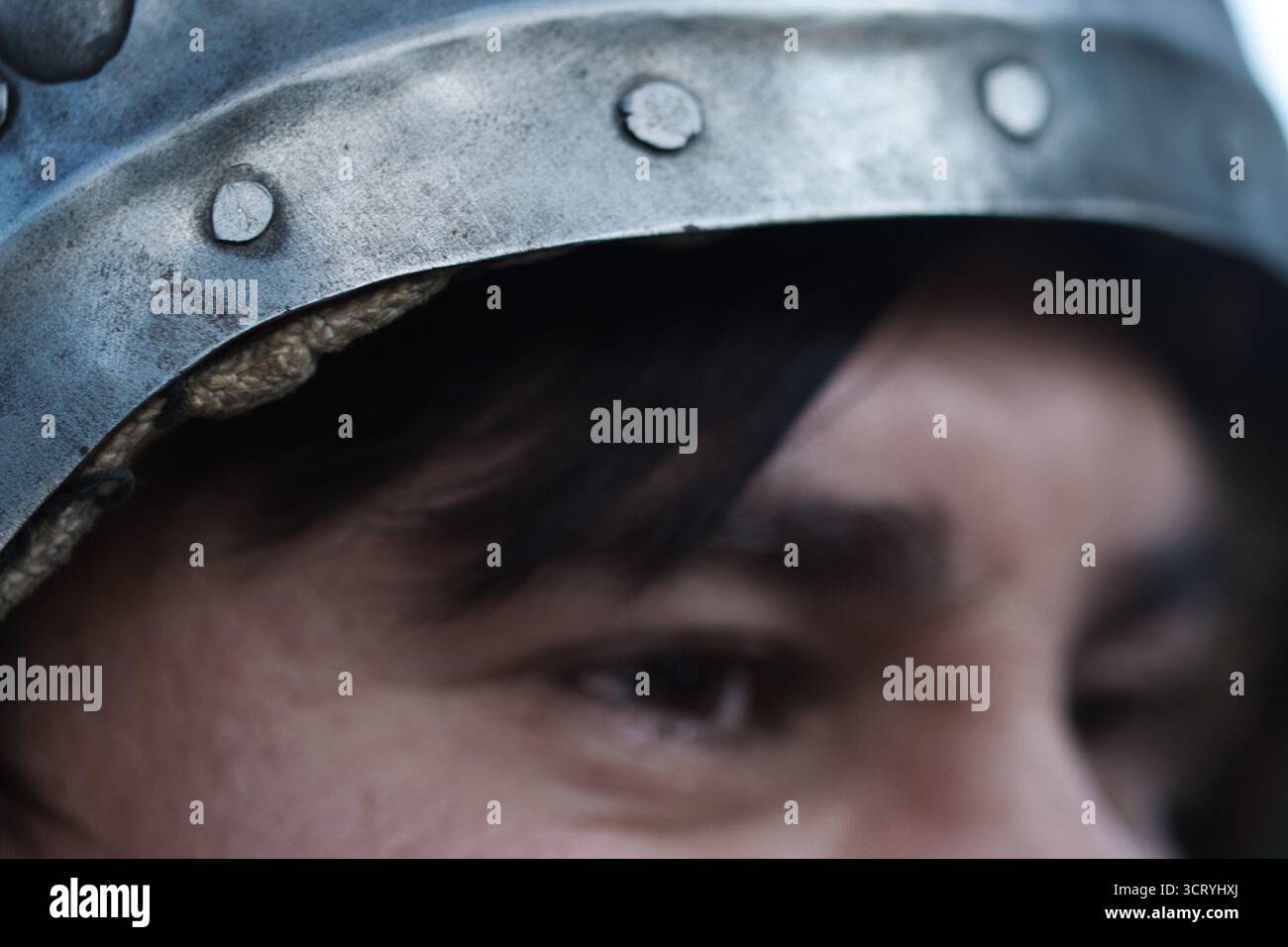 Primo piano di un uomo in armatura medievale che urla con intensità durante una rievocazione o una scena di battaglia. L'espressione drammatica e il casco. Foto Stock Primo piano di un uomo in armatura medievale che urla con intensità durante una rievocazione o una scena di battaglia. L'espressione drammatica e il casco. Foto Stock