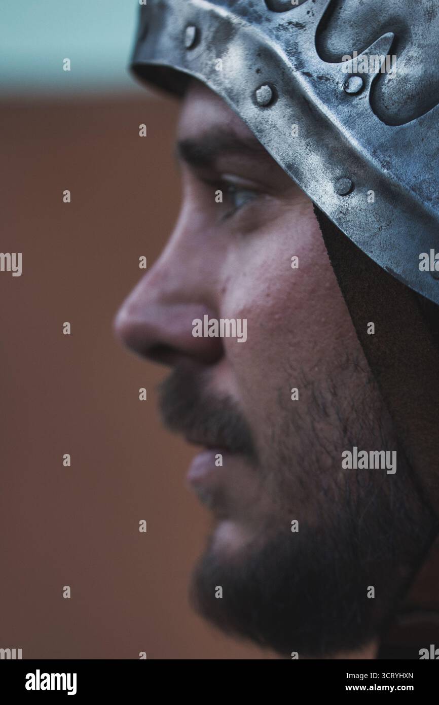 Primo piano di un uomo in armatura medievale che urla con intensità durante una rievocazione o una scena di battaglia. L'espressione drammatica e il casco. Foto Stock Primo piano di un uomo in armatura medievale che urla con intensità durante una rievocazione o una scena di battaglia. L'espressione drammatica e il casco. Foto Stock