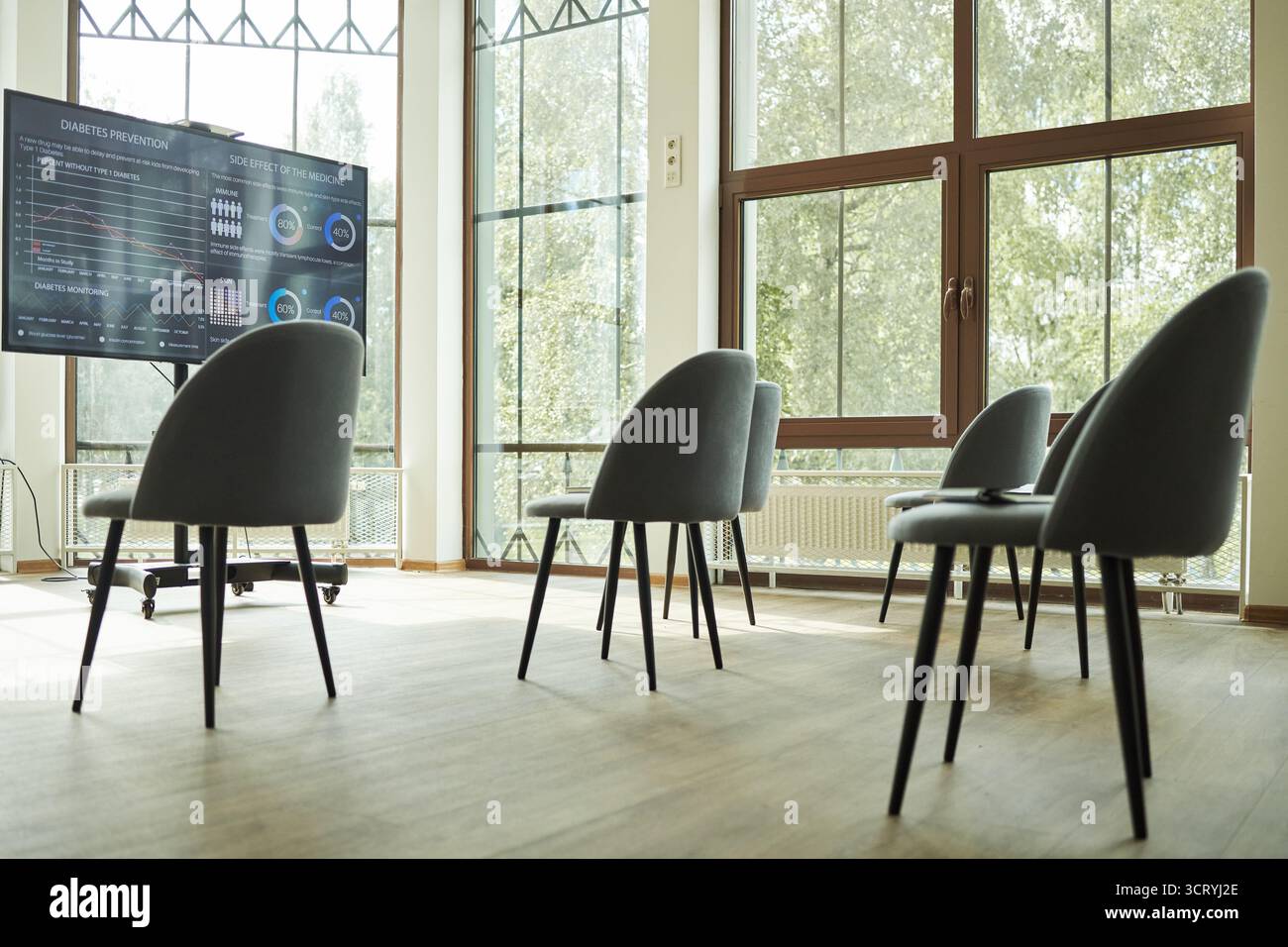 Moderna sala conferenze vuota con diverse sedie disposte davanti a un grande schermo digitale, che mostra grafici medici e grafici relativi alla prevenzione del diabete e alla scienza della resilienza Foto Stock