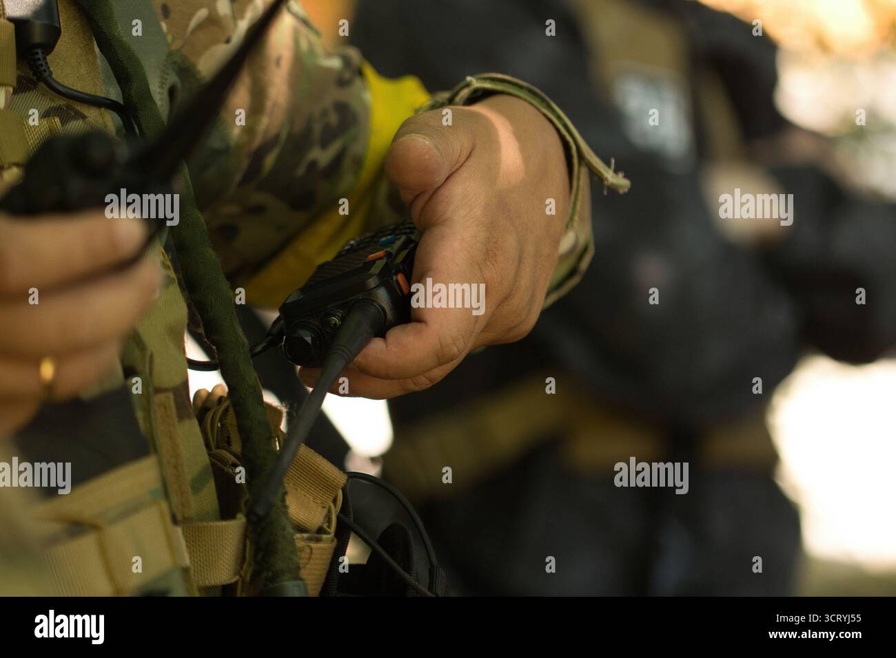 La mano di un soldato regge una radio militare, simboleggiando la comunicazione e il coordinamento sul campo. Foto Stock
