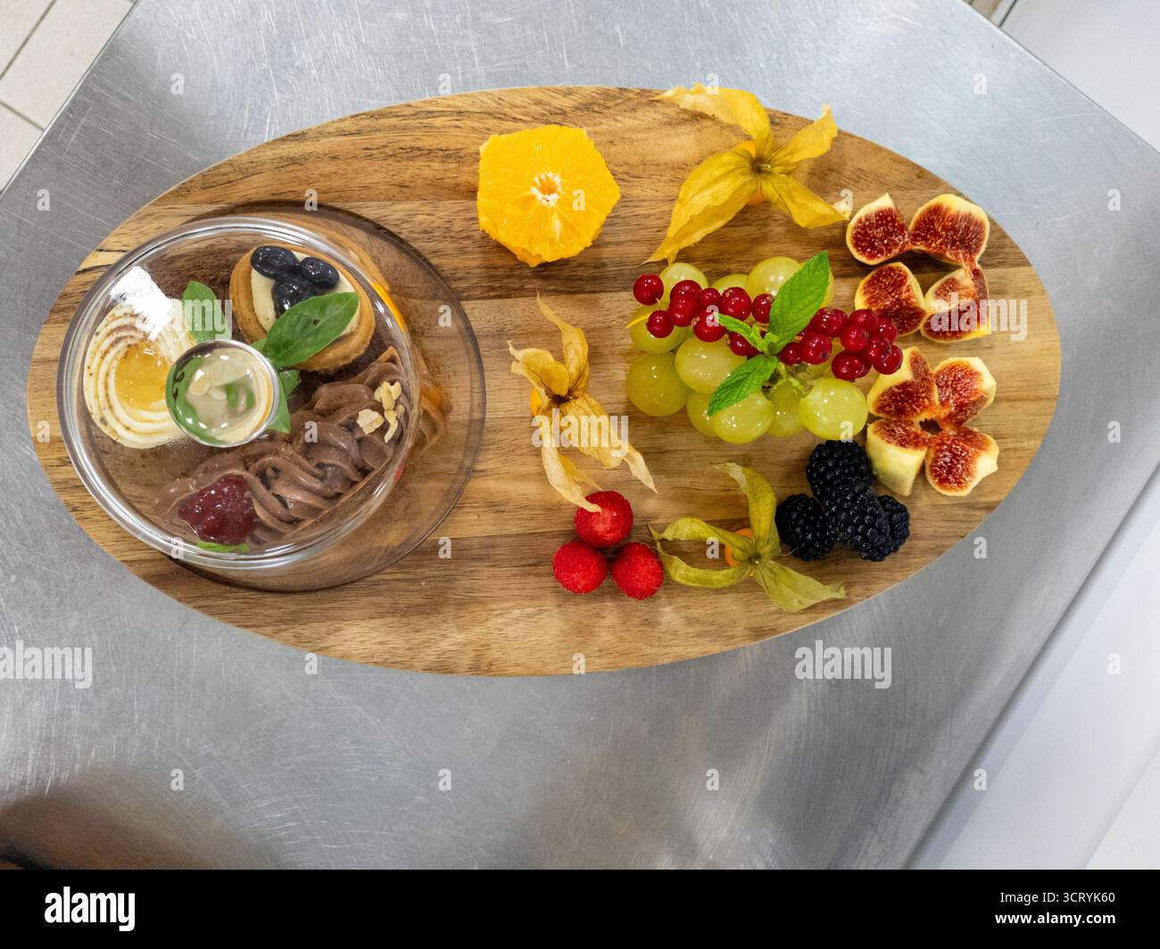 Vista dall'alto verso il basso di un dessert gourmet e un piatto di frutta su una tavola di legno. Una bella disposizione di frutti di bosco freschi, fichi, uva e pasticcini, perfetta Foto Stock