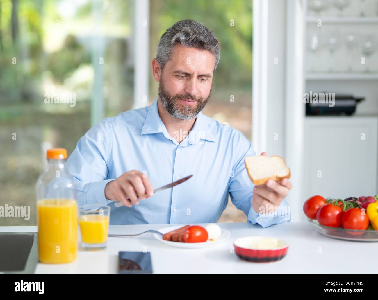 Un uomo fa colazione in cucina una mattina. l'uomo degli anni '40 ama il cibo fresco al tavolo della cucina. Un uomo mangia cereali e frutta in cucina. A ragazzo piace Foto Stock