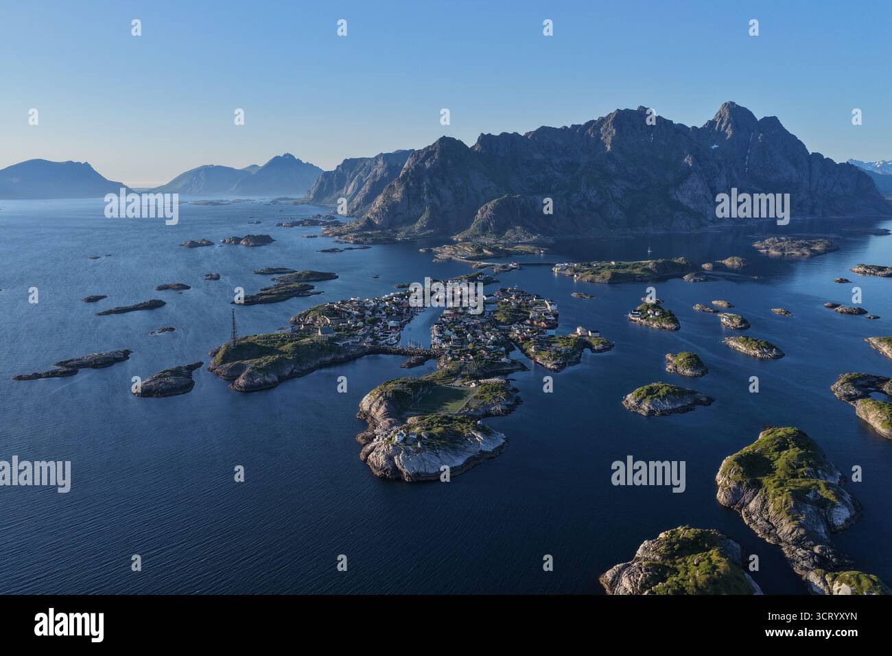 Il paesaggio delle isole Lofoten mostra un tradizionale villaggio di pescatori circondato dal mare e da molti piccoli isolotti, con aspre montagne sullo sfondo Foto Stock