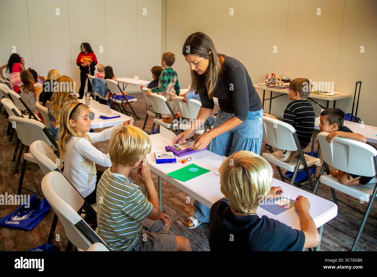 In un evento di formazione religiosa in un Dana Point, CA, chiesa cattolica, un genitore volontario distribuisce forniture d'arte ai bambini incaricati di illustrare la loro fede Foto Stock