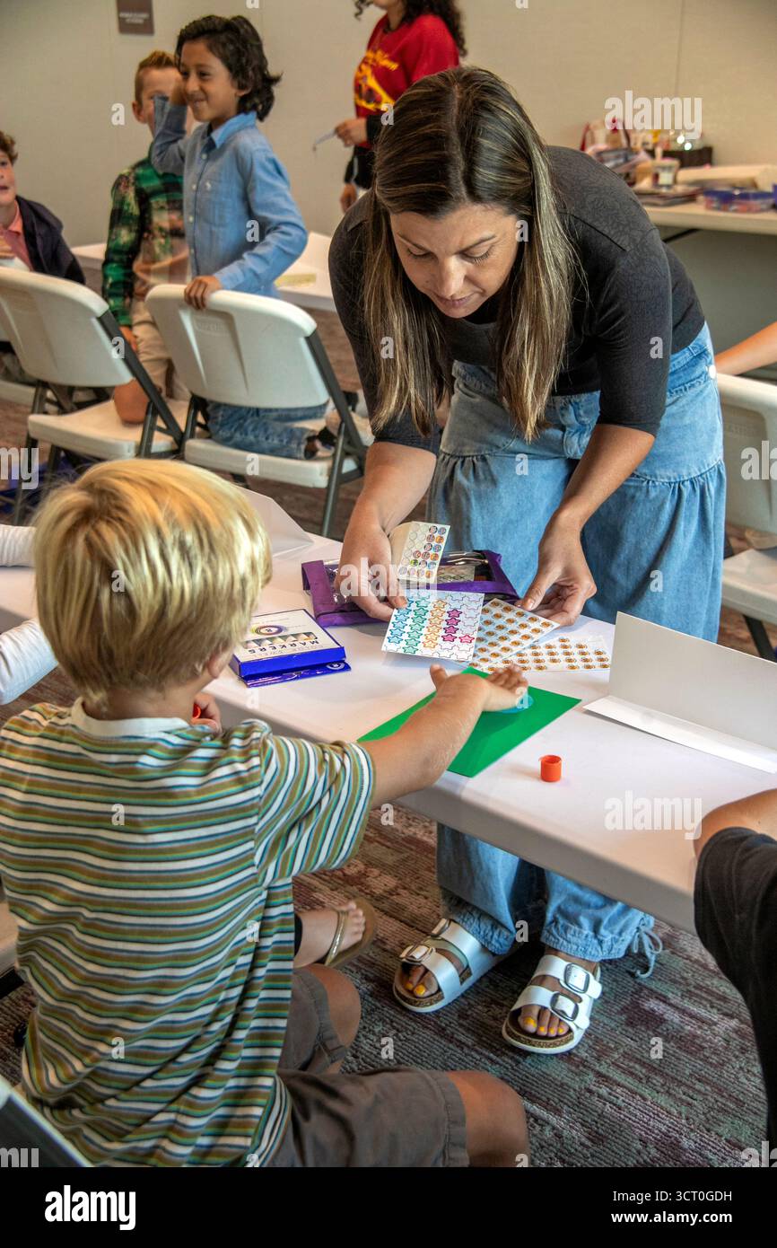 In un evento di formazione religiosa in un Dana Point, CA, chiesa cattolica, un genitore volontario distribuisce forniture d'arte ai bambini incaricati di illustrare la loro fede Foto Stock