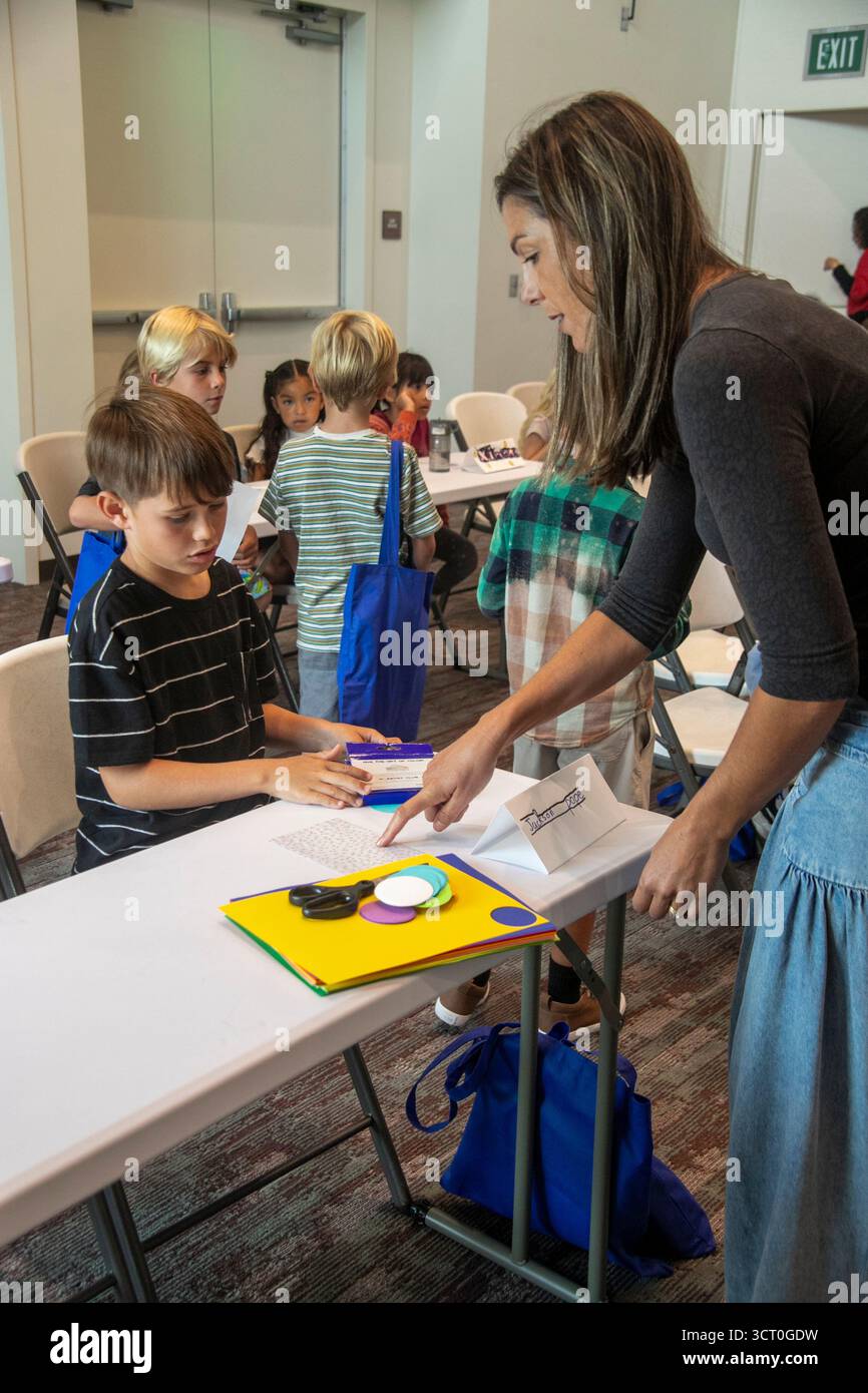 In un evento di formazione religiosa in un Dana Point, CA, chiesa cattolica, un genitore volontario distribuisce forniture d'arte ai bambini incaricati di illustrare la loro fede Foto Stock