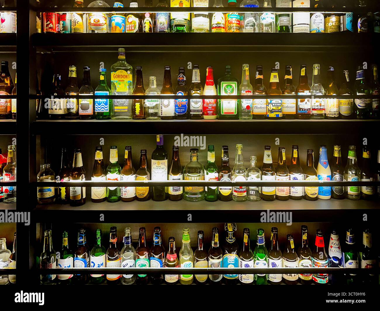 Una varietà di bottiglie di birra esposte sugli scaffali di un negozio di liquori con diverse etichette e confezioni colorate sotto l'illuminazione luminosa di ipoh malaysia Foto Stock