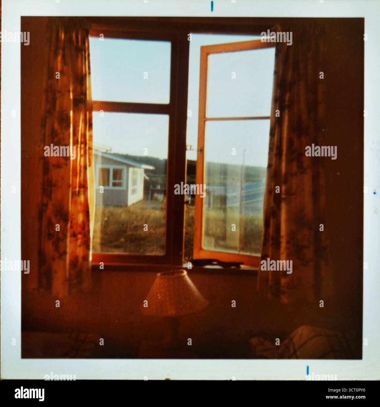 Immagine analogica di finestre con cornici in legno e vecchie tende. Si affaccia su una camera da letto in una casa sulla spiaggia di metà secolo in nuova Zelanda, con la luce del sole nel tardo pomeriggio Foto Stock