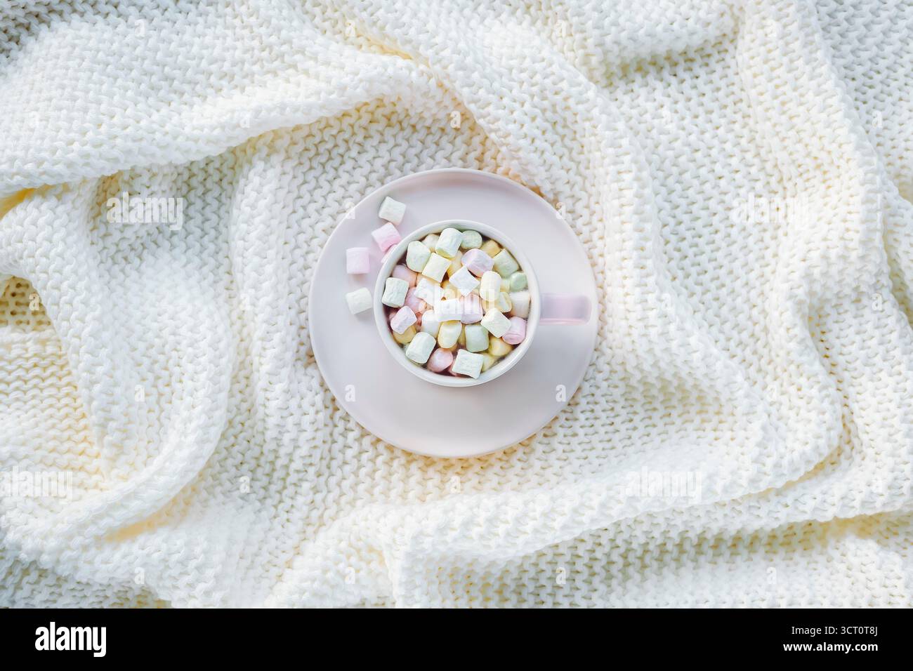 Tazza rosa con marshmallow pastello su morbida coperta a maglia bianca. Accogliente natura morta invernale, vista dall'alto, letto piatto. Foto Stock