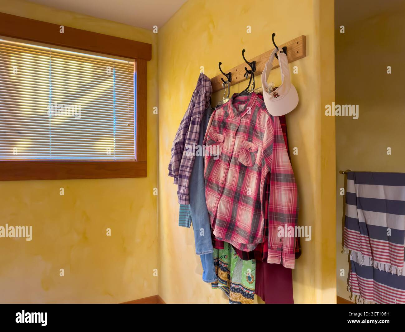 Vestiti appesi ai ganci, asciugamano a righe su un rack, scale ombreggiate nella finestra di una camera d'albergo luminosa con pareti in mattoni gialli, Colorado, USA. Foto Stock