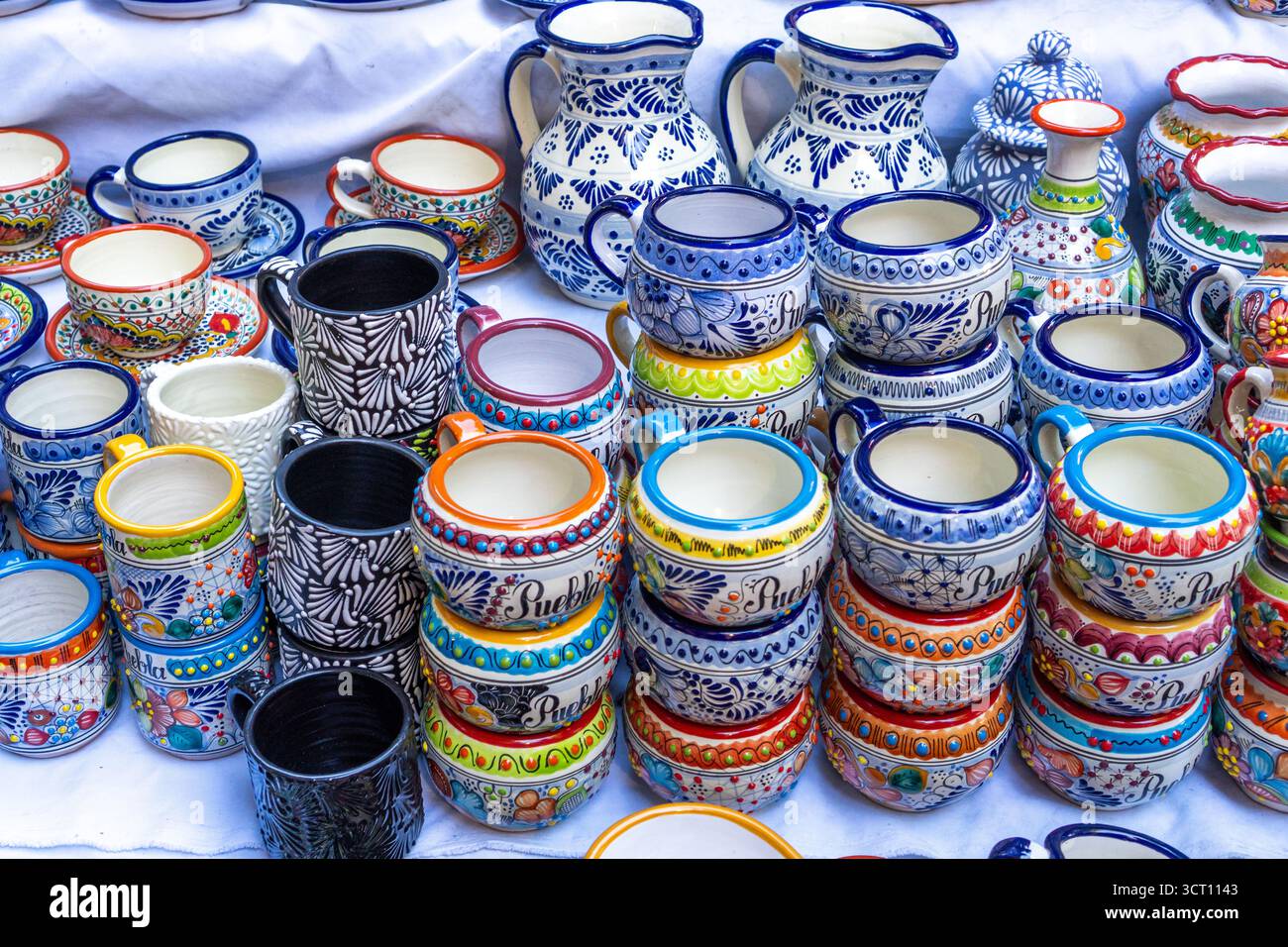 Un tavolo pieno di tazze e ciotole in ceramica colorata. Le tazze e le ciotole sono di varie forme e dimensioni. Città di Puebla, Messico, artigianato Foto Stock