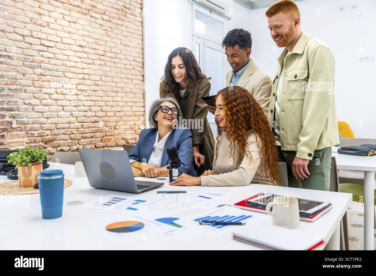 Professionisti aziendali diversi che condividono idee e ridono insieme durante una sessione di registrazione di podcast collaborativa o una riunione di team in un ufficio moderno Foto Stock