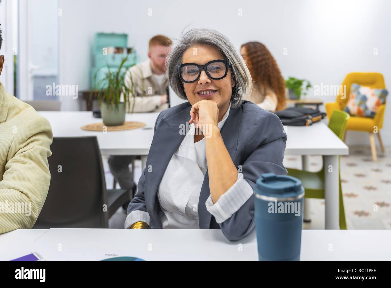 Donna d'affari esperta sorridente con fiducia durante una riunione in un ufficio moderno, rappresentando professionalità, leadership e successo Foto Stock