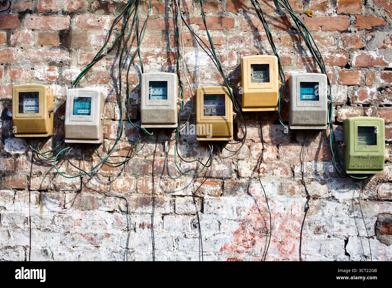 Fila di contatori elettrici e fili esposti su una parete di mattoni a Kushtia, Bangladesh, che illustrano le infrastrutture elettriche urbane. Foto Stock