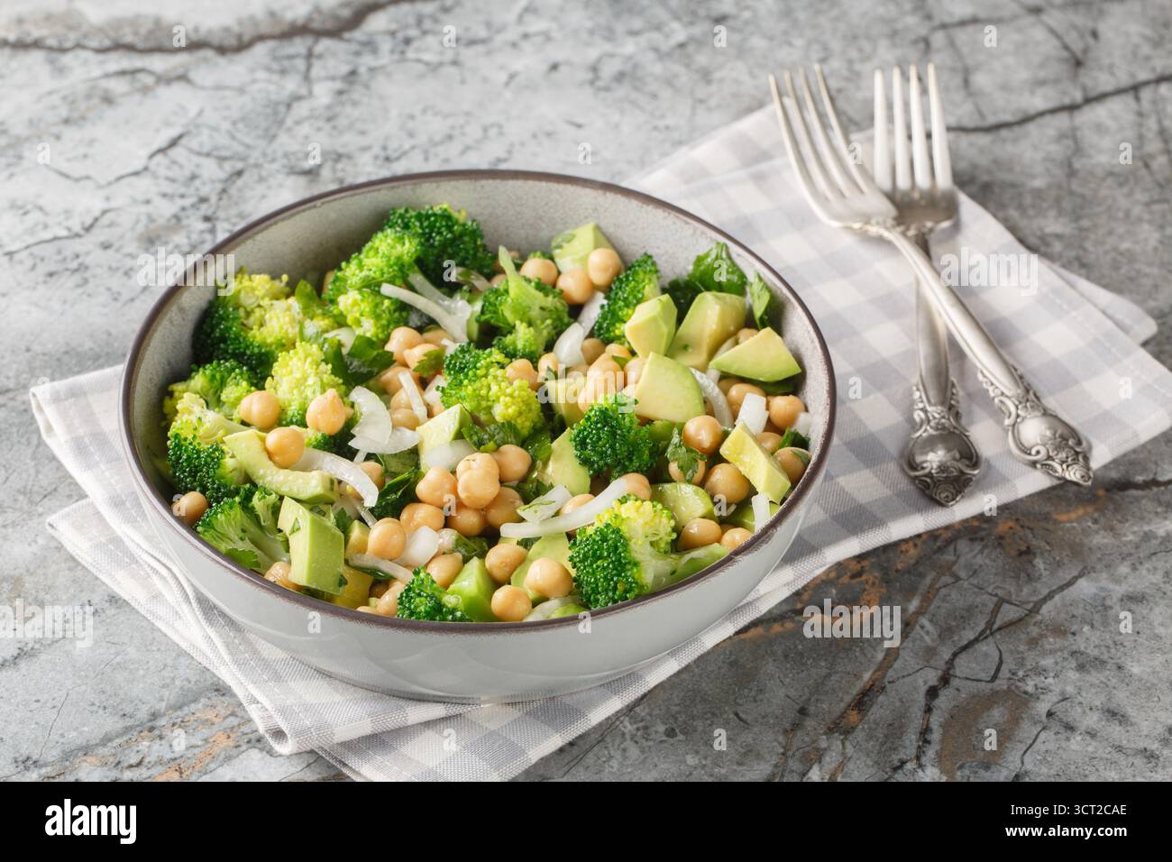 primo piano di un'insalata dietetica di broccoli, ceci, avocado, cipolla e prezzemolo in un recipiente su un tavolo. Orizzontale Foto Stock