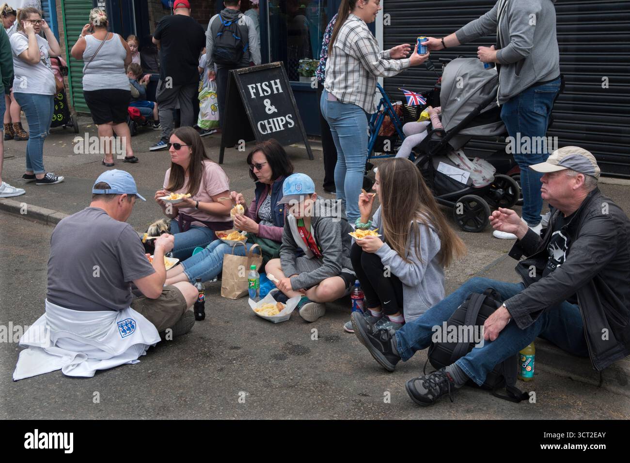 Pasto fast food Fish and Chip. Persone, gruppo di famiglie sedute sul marciapiede a mangiare Fish N Chips. Corby. Northamptonshire, Inghilterra 3 giugno 2022 2020s UK HOMER SYKES Foto Stock