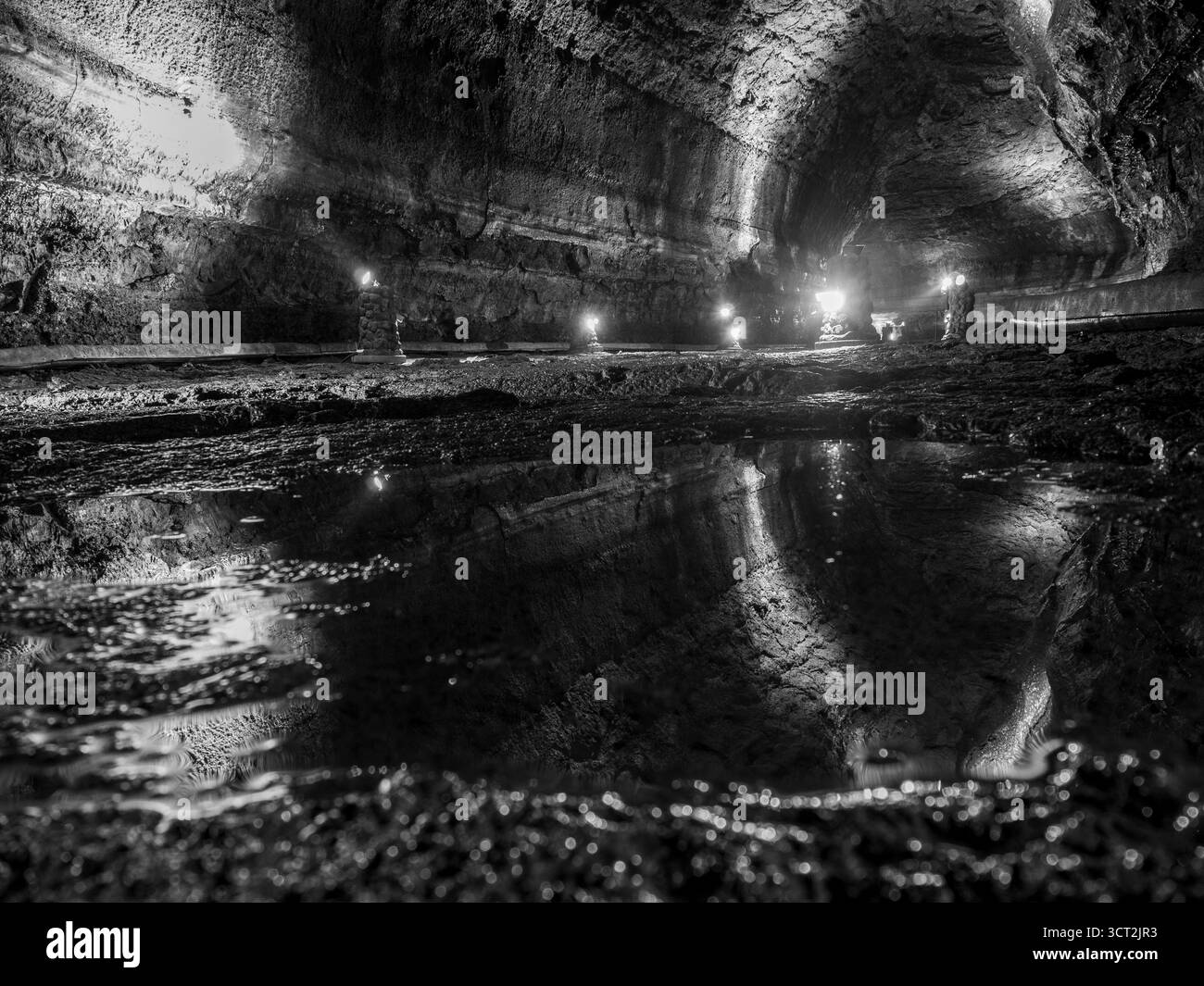 Nella Grotta di Mangjanggul, Jeju, una figura solitaria in una si erge davanti al tunel sul pavimento roccioso accanto a una pozzanghera che riflette la grotta di lava tutta litata Foto Stock
