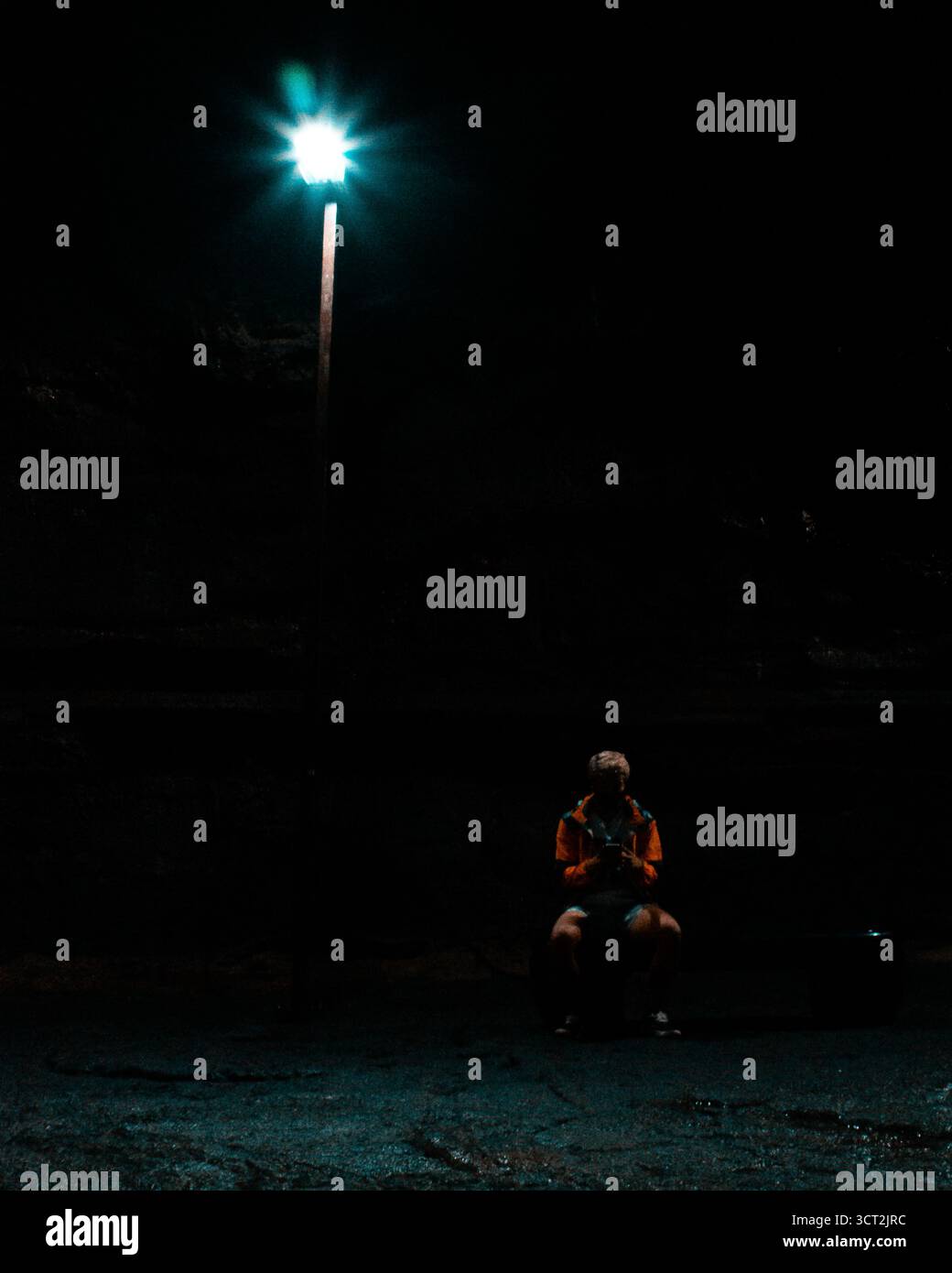 Nella Grotta di Mangjanggul, Jeju, una figura solitaria in un impermeabile giallo brillante si trova accanto a un lampione sul pavimento roccioso, avvolto da ombre profonde. Foto Stock