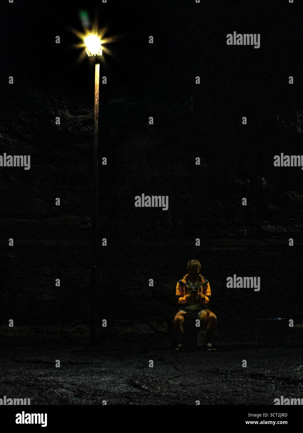 Nella Grotta di Mangjanggul, Jeju, una figura solitaria in un impermeabile giallo brillante si trova accanto a un lampione sul pavimento roccioso, avvolto da ombre profonde. Foto Stock