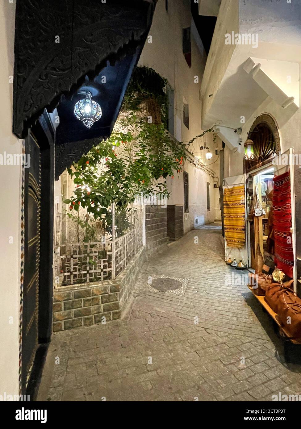Vicoli stretti e vivaci scenari di mercato a Tangeri, Marocco. Architettura tradizionale, pareti blu, prodotti artigianali, lanterne calde. 2 OTTOBRE 2025 Foto Stock