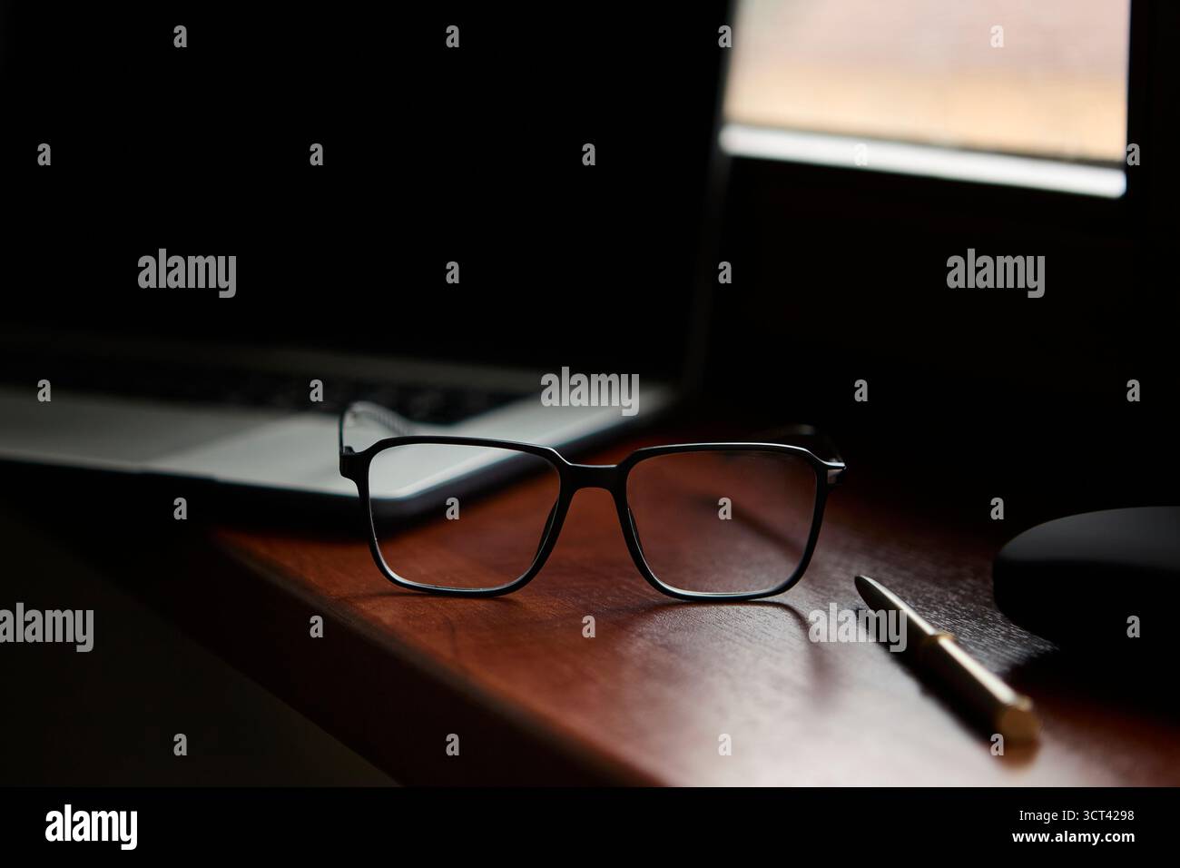Occhiali da vista con penna su una superficie lucida accanto al laptop con sfondo sfocato. Ambiente professionale pulito per concetti di stile di vita aziendale. Foto Stock