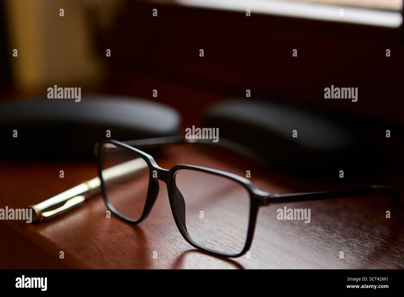 Un paio di occhiali poggia vicino a una penna dorata su una scrivania in legno lucido. Un laptop sullo sfondo aggiunge un'atmosfera professionale moderna all'ambiente di lavoro W Foto Stock