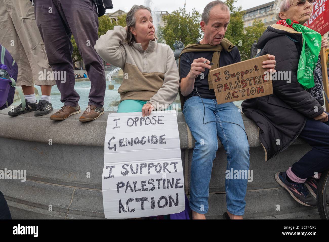 Trafalgar Square, Londra, Regno Unito. 4 ottobre 2025. Un gruppo di manifestanti seduti intorno a una fontana pubblica in una piazza urbana, tenendo dei cartelli a sostegno dell'azione palestinese e opponendosi al genocidio. La protesta presenta cartelli visibili, abbigliamento solidale e impegno civico collettivo. Difendere le nostre giurie tenere una protesta non violenta contro l’azione diretta a Trafalgar Square a Londra. L'obiettivo della protesta è quello di revocare il divieto di azione contro la Palestina, che è stato bandito come gruppo terroristico nel luglio 2025 ai sensi della legge sul terrorismo del Regno Unito del 2000. Penelope Barritt/Alamy Live News Foto Stock