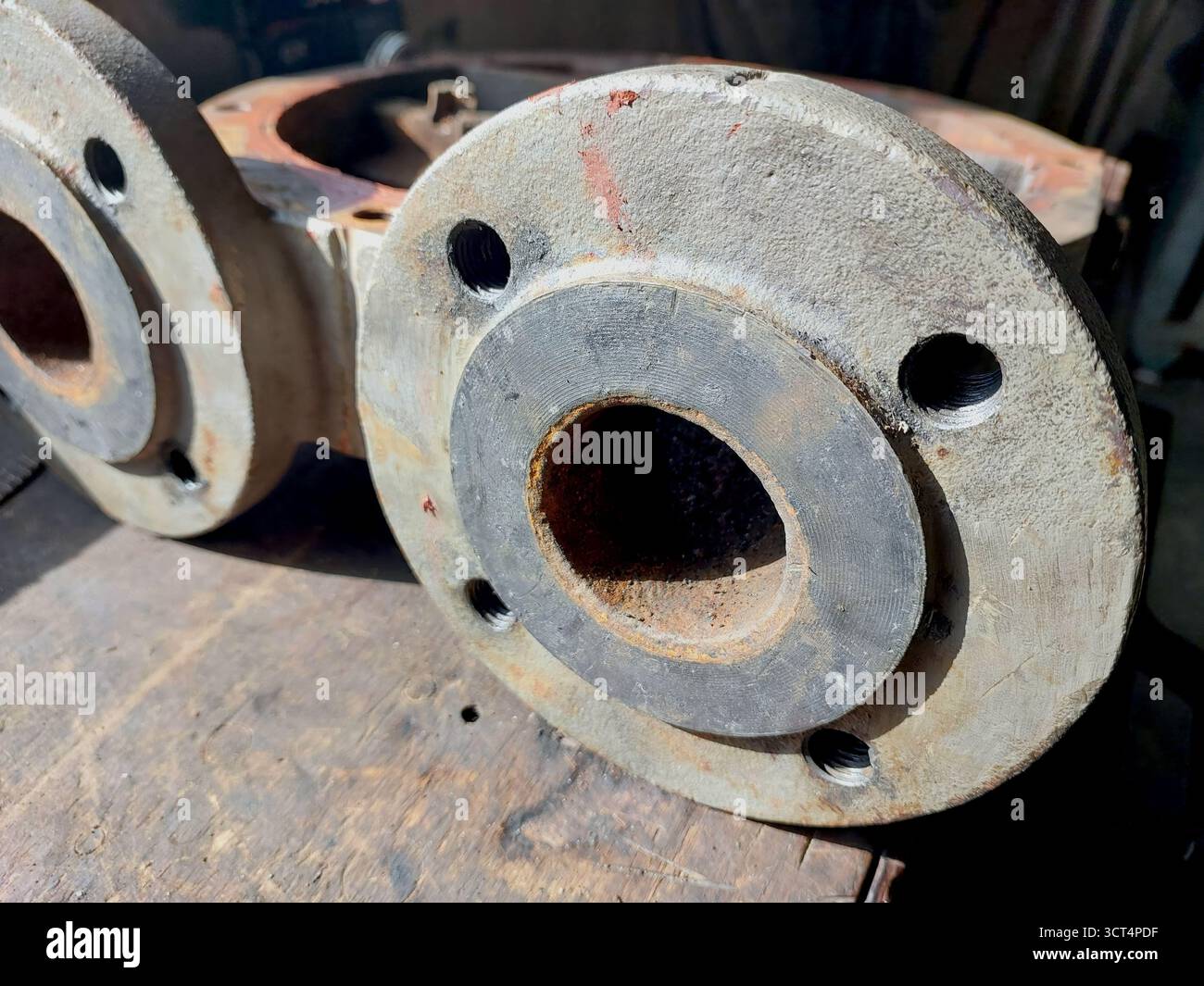 Vista ravvicinata delle flange del corpo pompa in ghisa, rivelando la struttura della superficie e i fori di montaggio, in legno intemprato in un ambiente di officina. Foto Stock