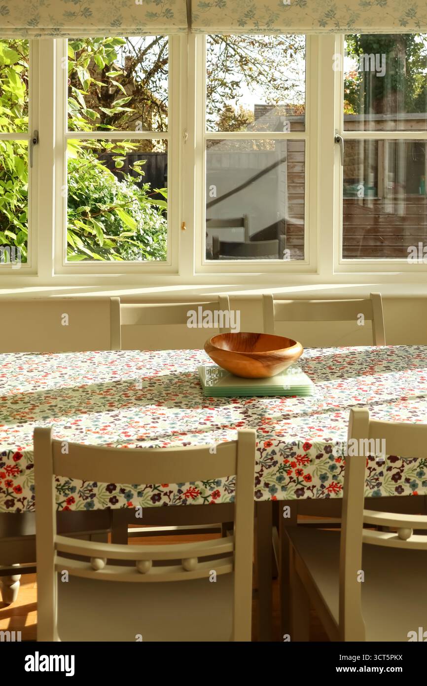 Tavolo da pranzo con tovaglia floreale e ciotola in legno, che cattura la luce naturale del sole attraverso una finestra. Campagna dei Cotswolds, Inghilterra Foto Stock