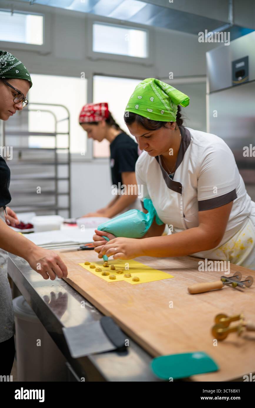 Piacenza, Italia - 25 settembre 2025 le giovani donne realizzano tortelli artigianali in una cucina italiana professionale che mette in mostra la produzione alimentare regionale Foto Stock