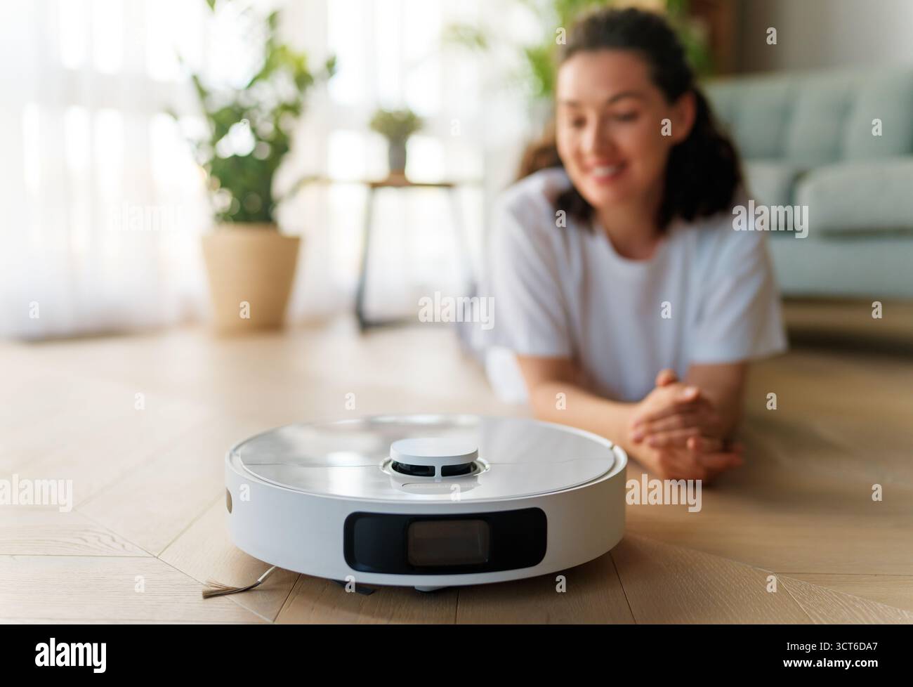 Aspirapolvere robotizzato bianco su pavimento in legno. Tecnologia di pulizia intelligente Foto Stock