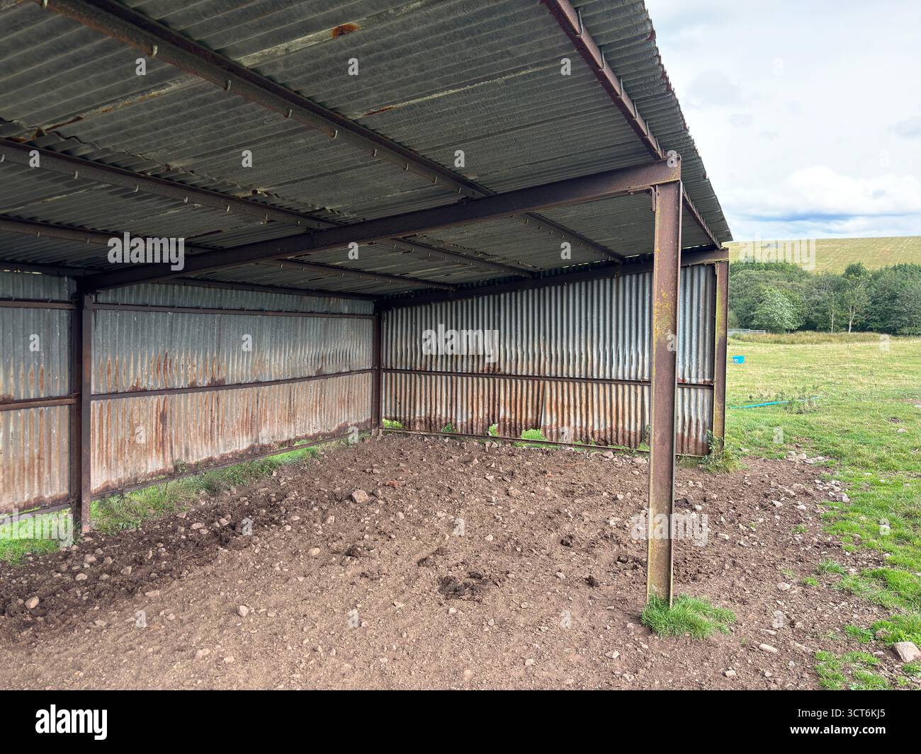 Antica struttura arrugginita del fienile delle mucche su pendii collinari con erba e rocce nel paesaggio scozzese. Foto Stock