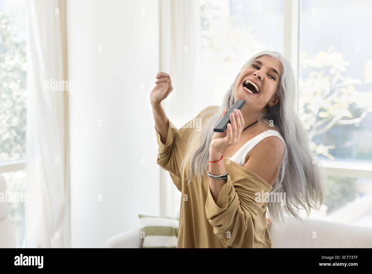 Felice eccitata cantante latina anziana che canta a casa Foto Stock