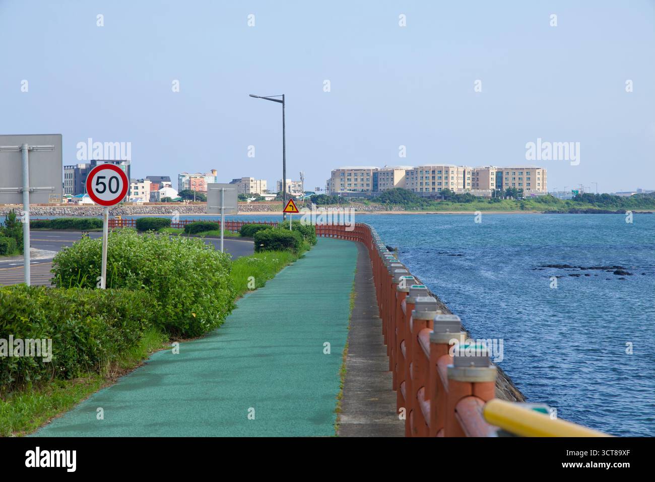 Una strada costiera dipinta segue il lungomare vicino al villaggio di Seongsan, con appartamenti bassi e strade sul lungomare che si snodano lungo la baia accanto al sh Foto Stock