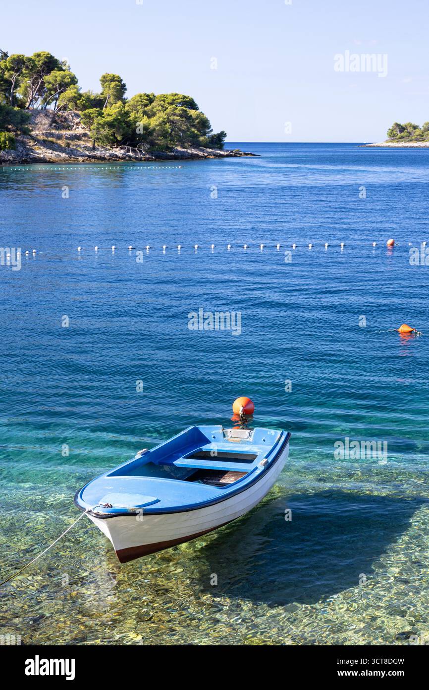 Una tranquilla scena di una barca blu che galleggia dolcemente su acque blu calme, con una linea curva di boe e isole lontane sotto un cielo luminoso e limpido. Foto Stock