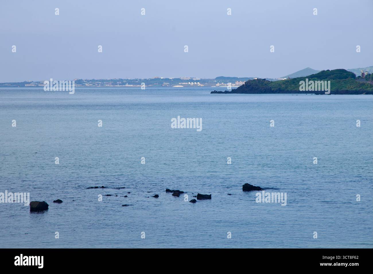 Guardando attraverso la tranquilla baia di Hado verso una costa lontana, bassi promontori ed edifici fiancheggiano l'orizzonte sopra il Mare Orientale. Foto Stock