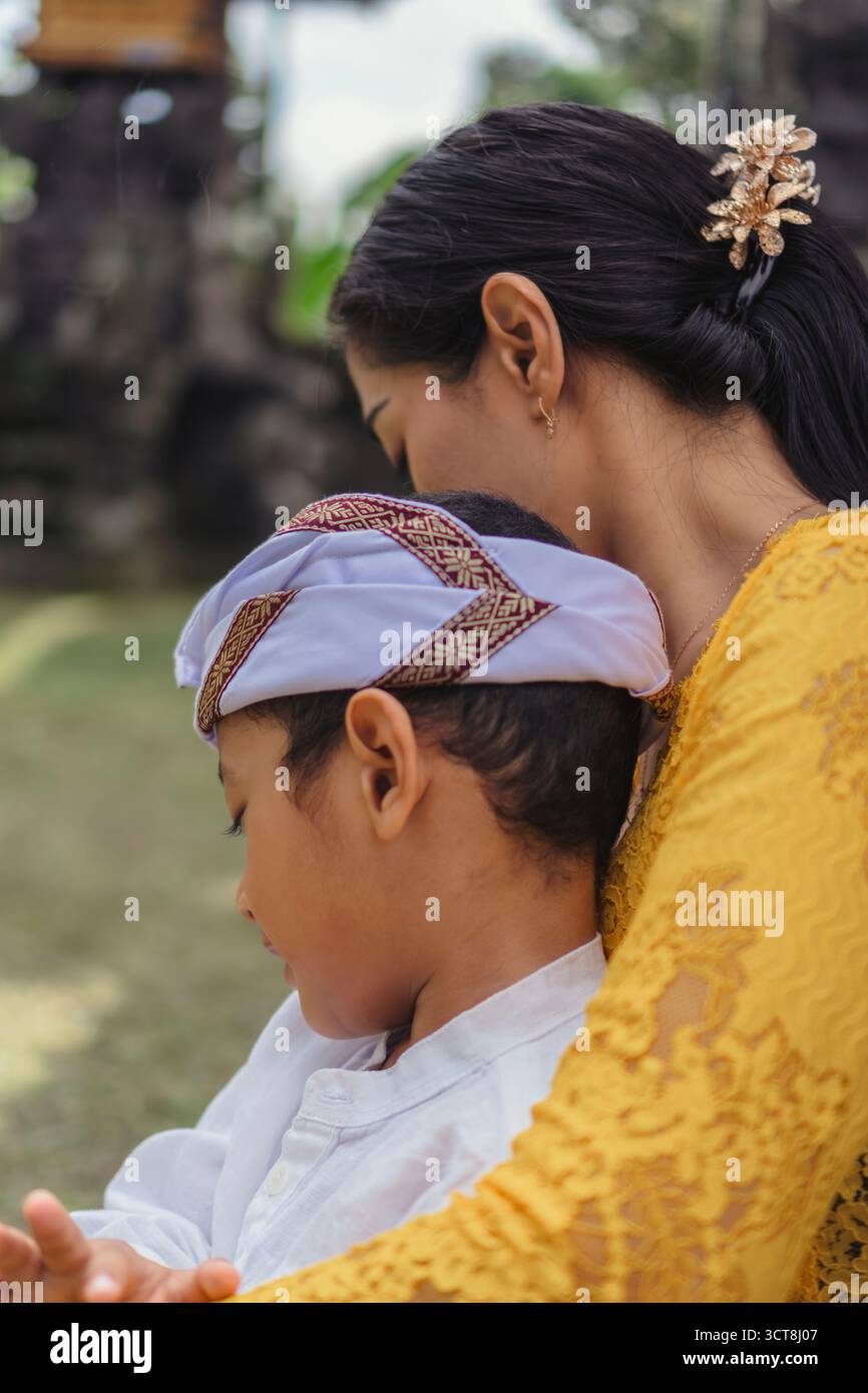 Una madre balinese che abbraccia da vicino suo figlio durante le preghiere del tempio Galungan. Foto Stock