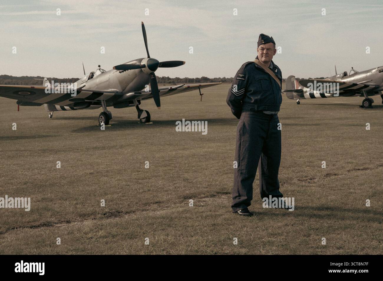 Sergente della RAF in uniforme d'epoca accanto agli aerei Spitfire d'epoca presso l'aeroporto di Duxford Foto Stock