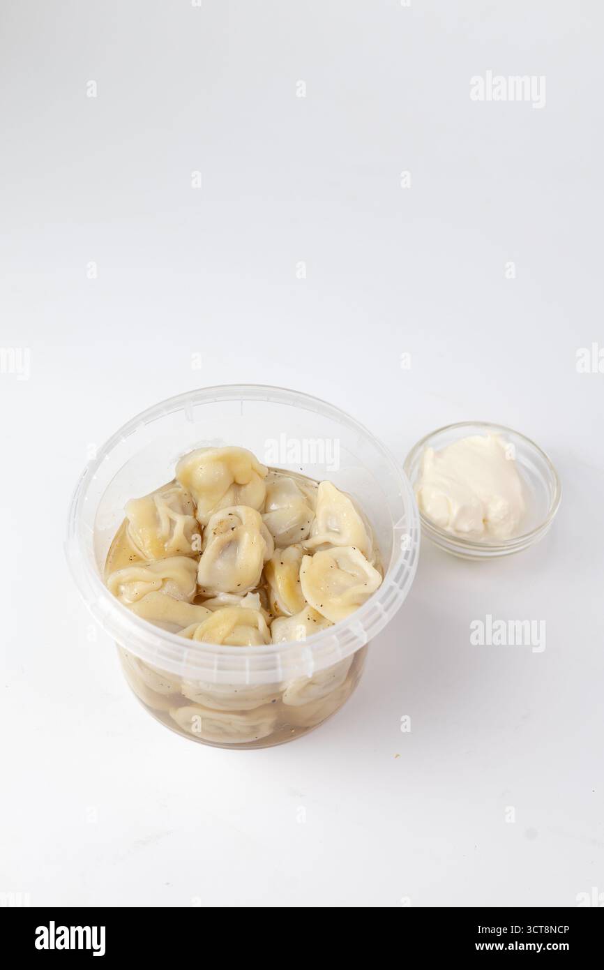 La cottura a vapore degli gnocchi fatti in casa riposa in un contenitore di plastica trasparente, leggermente condito e abbinato a un piccolo recipiente di panna acida cremosa. Foto Stock