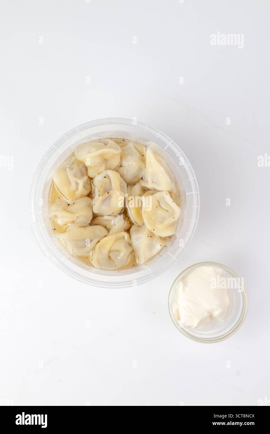 La cottura a vapore degli gnocchi fatti in casa riposa in un contenitore di plastica trasparente, leggermente condito e abbinato a un piccolo recipiente di panna acida cremosa. Foto Stock