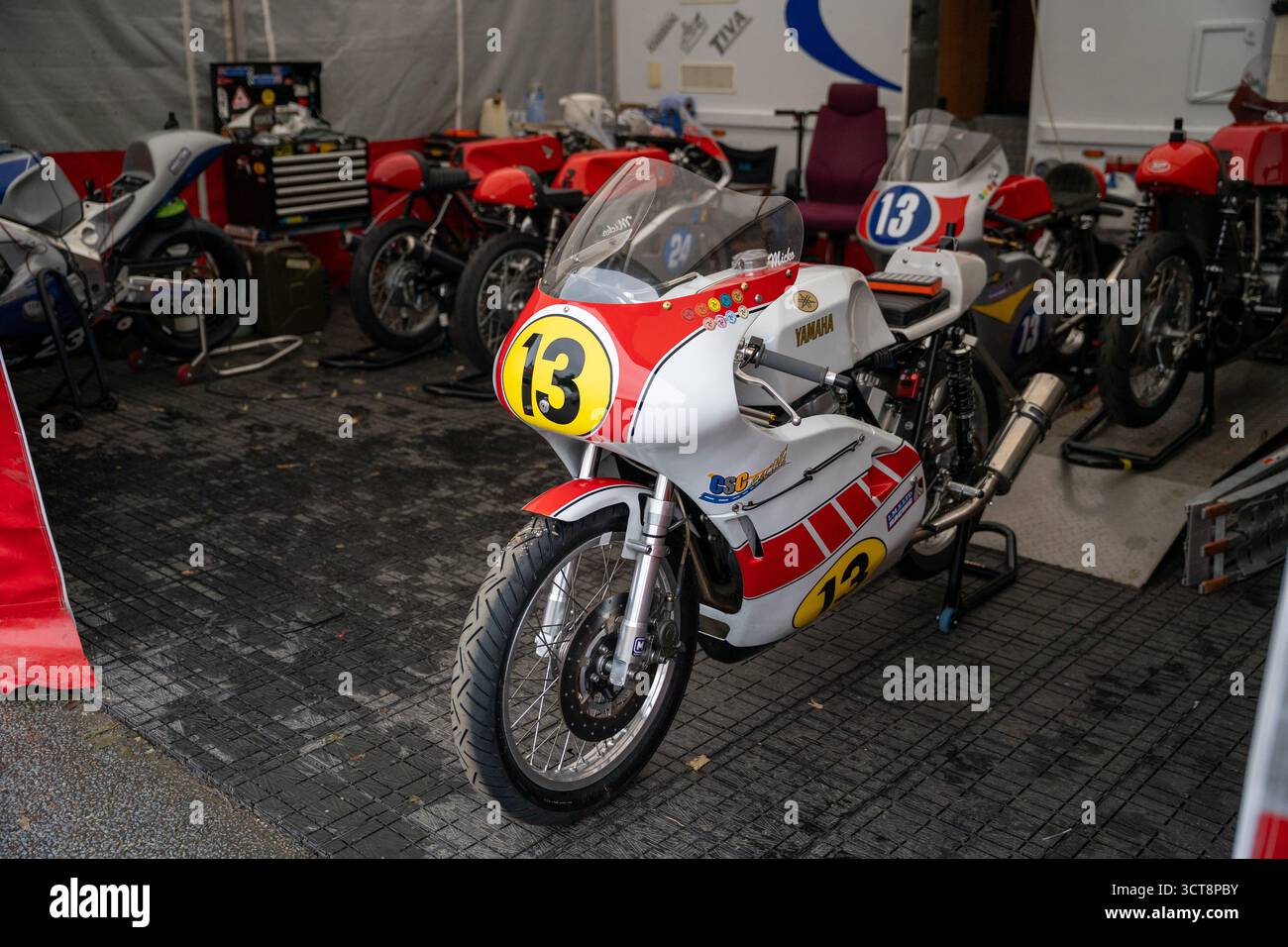 Motociclette da corsa classiche in garage paddock con numero 13 Yamaha in primo piano Foto Stock