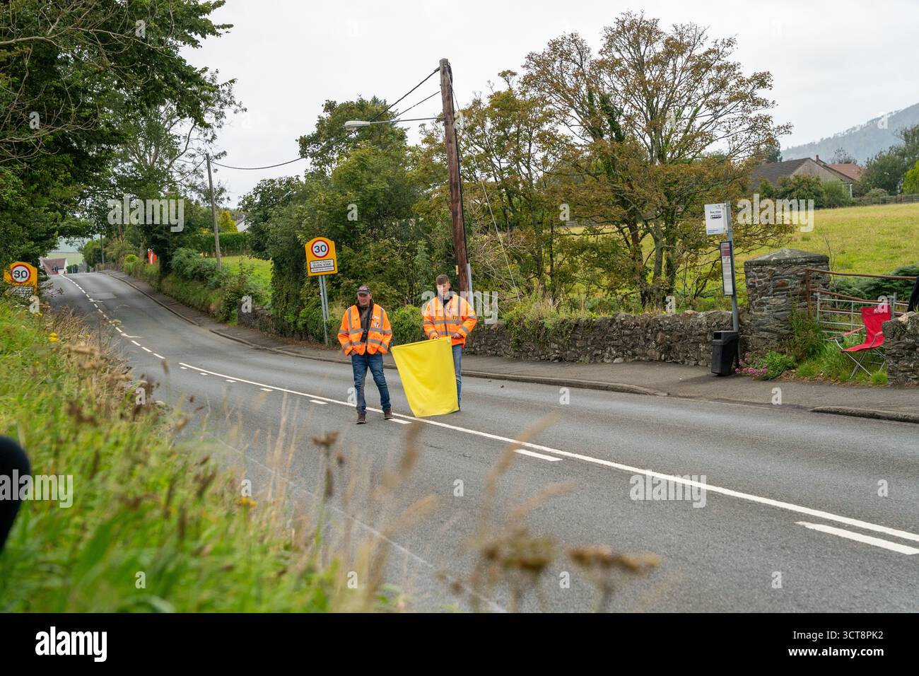 Lavoratori della strada in giacche ad alta visibilità che gestiscono il traffico sulla strada rurale dell'Isola di Man Foto Stock