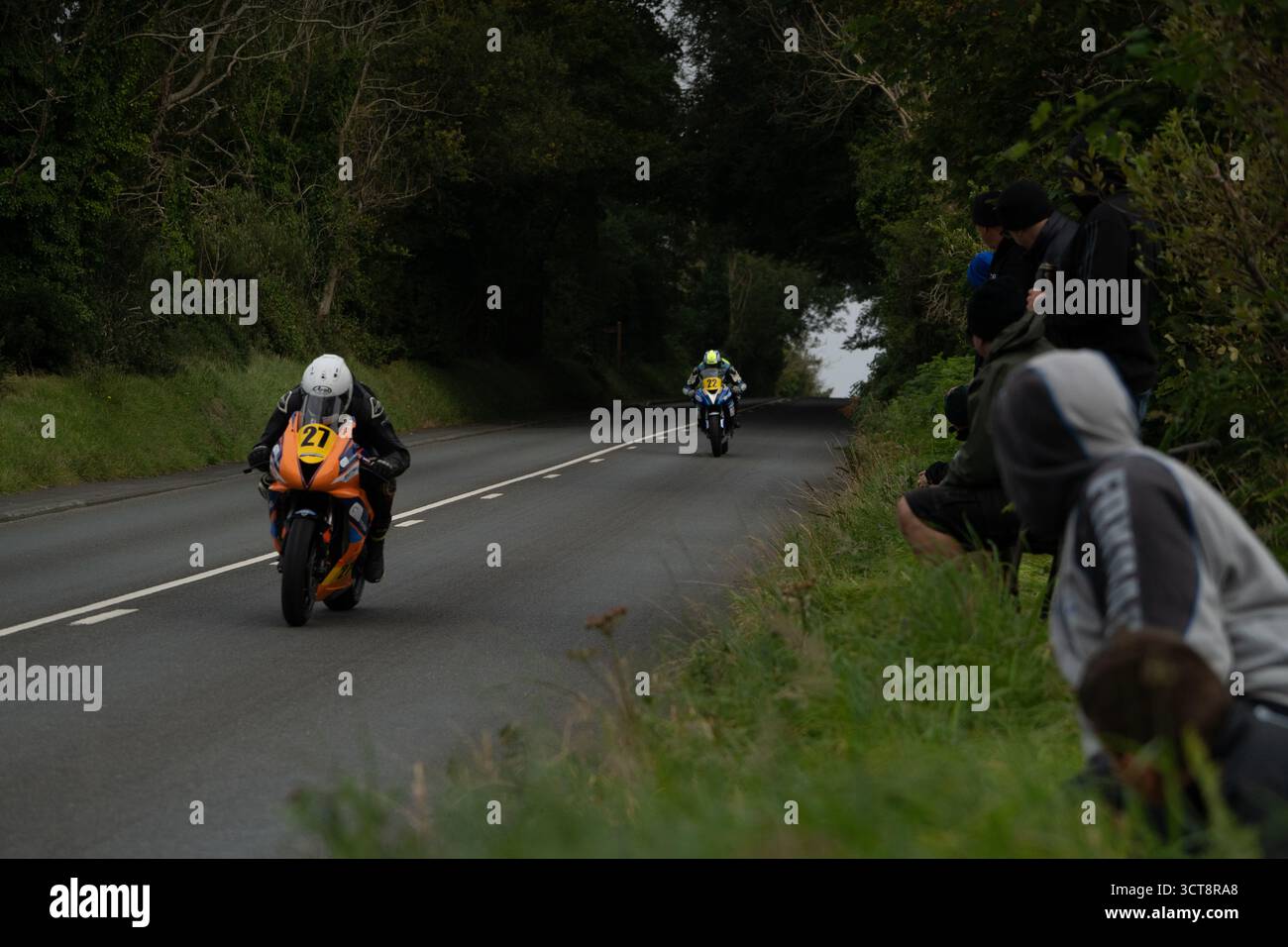Motociclette da corsa su strada di campagna con spettatori che guardano da Verge Foto Stock