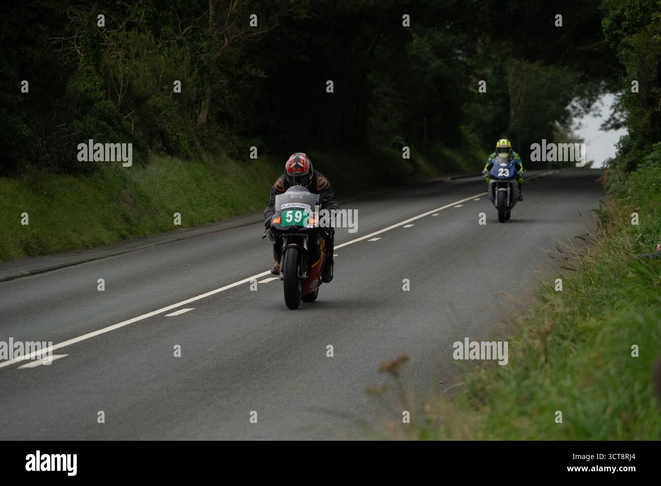 Due motociclette su una strada di campagna fiancheggiata da alberi e siepi Foto Stock
