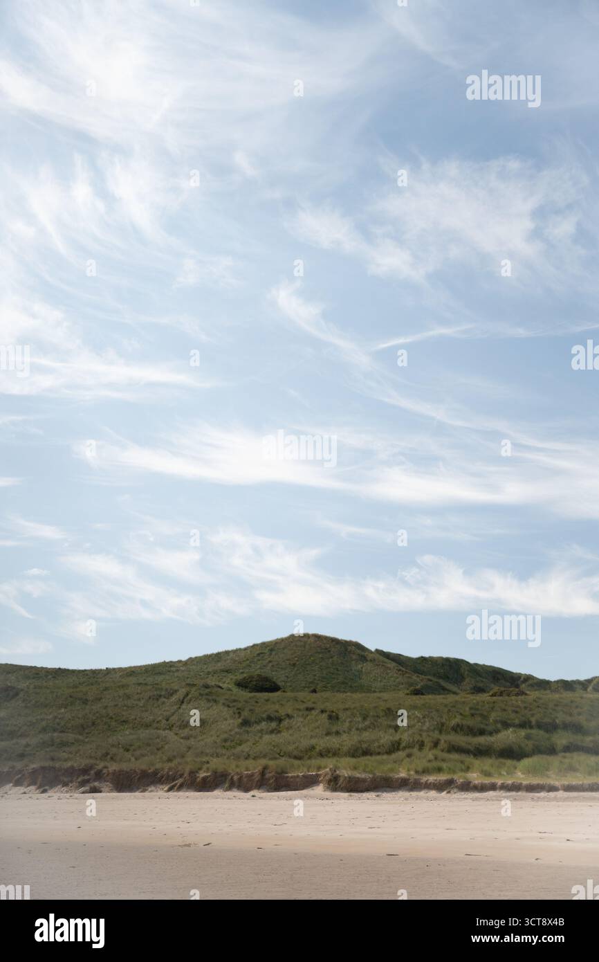 Paesaggio costiero con verdi colline e spiaggia sabbiosa sotto il cielo nuvoloso nel Northumberland Foto Stock