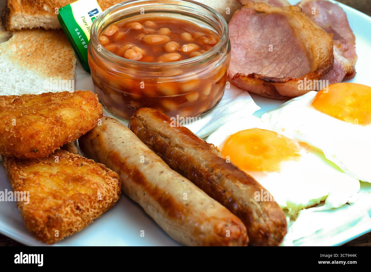 Gusta un'abbondante colazione all'inglese! Pane tostato, fagioli, salsiccia, uova, pancetta, e crocchette di hash - carburante per la giornata! Foto Stock